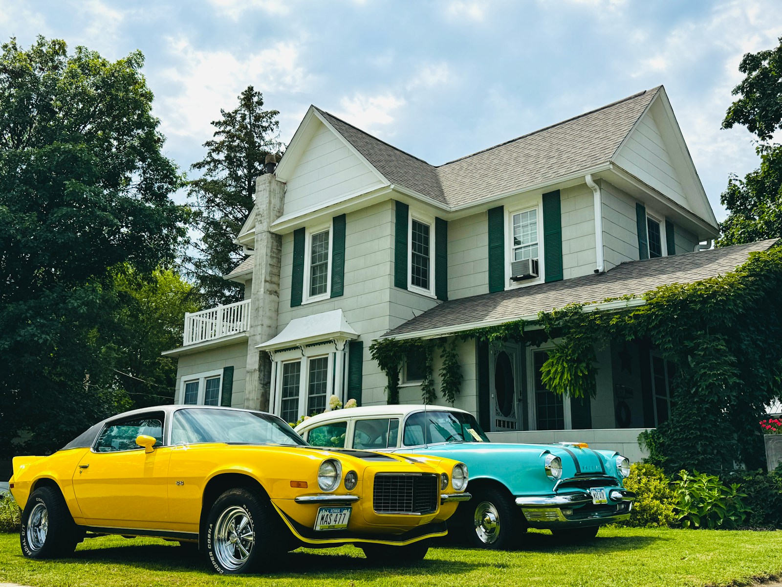 Two vintage cars parked in front of a large house, home & auto