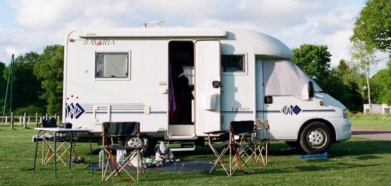 white and brown rv trailer on green grass field under white cloudy sky during daytime